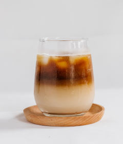 A two tone glass of Coconut Cacao Latte, placed on a wooden coaster